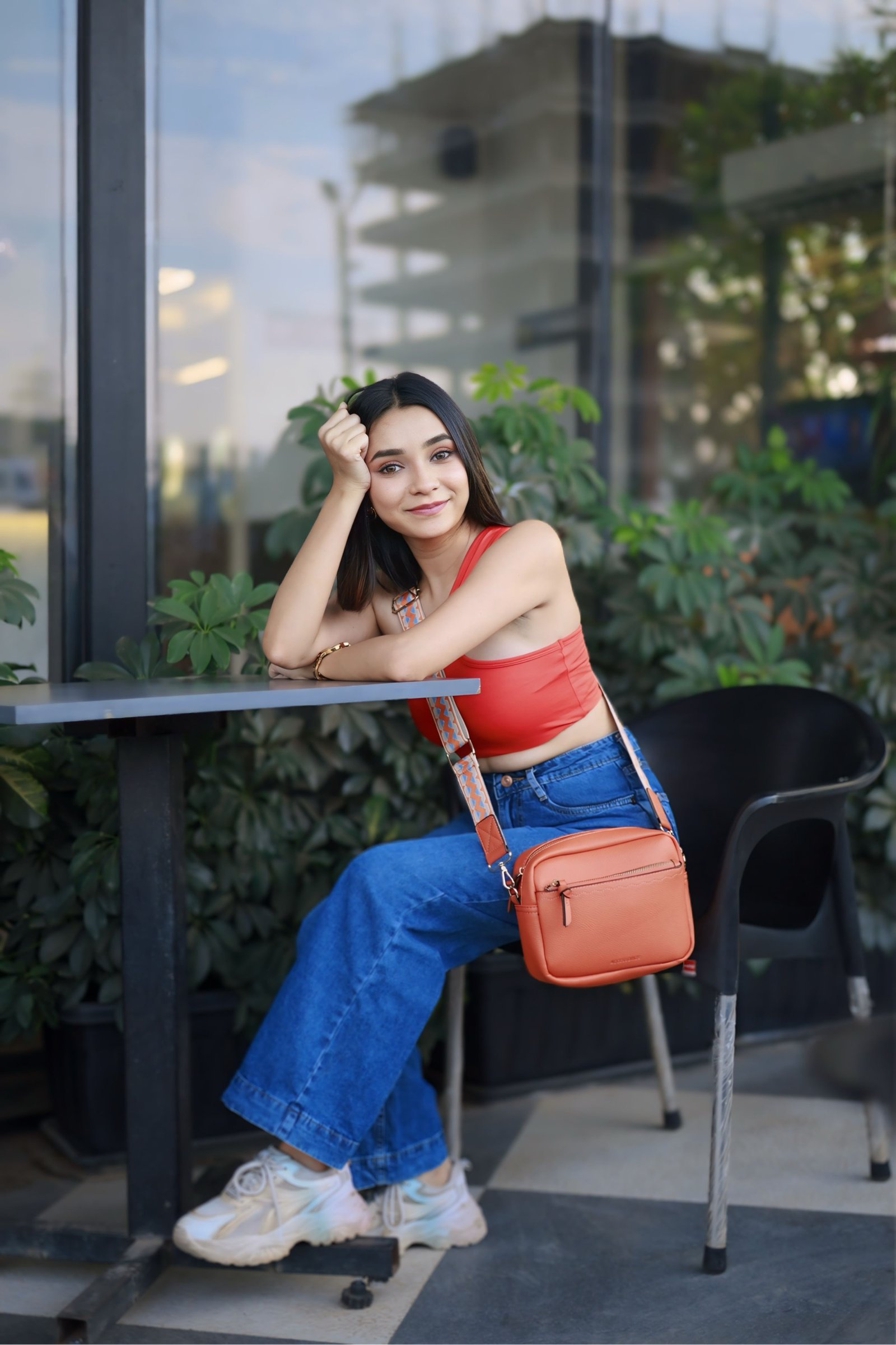 Hitakshi Chatterjee at a café table in a red crop top with an orange sling bag